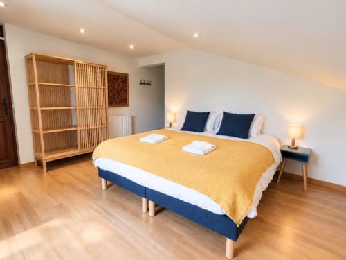 Chambre spacieuse de la Maison Héléna à Lain avec mobilier en bois, jeté jaune, lit bleu marine et vue sur la piscine