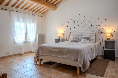 Chambre lumineuse aux Gîtes de Val à Cabannes avec stickers papillons, poutres en bois et vue sur le jardin