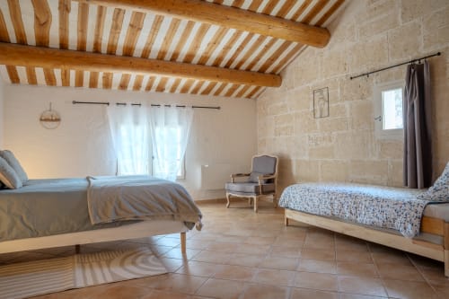 Chambre spacieuse aux Gîtes de Val avec poutres apparentes, deux lits, vue sur jardin et murs en pierre rustique