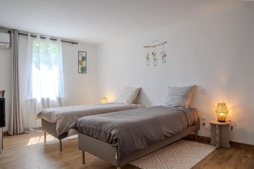 Chambre double moderne aux Gîtes de Val, Cabannes. Deux lits simples, lampes de chevet, bureau et fenêtre vue jardin