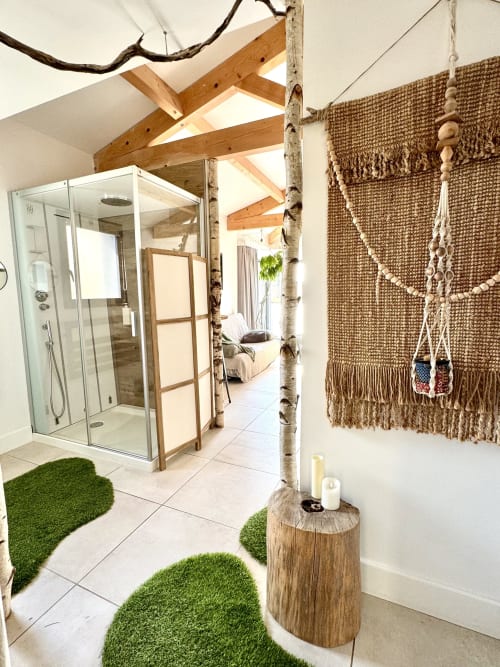 Luxury bathroom suite at Maison Florence Ivakno with glass shower, exposed beams, woven tapestry wall, and artificial grass