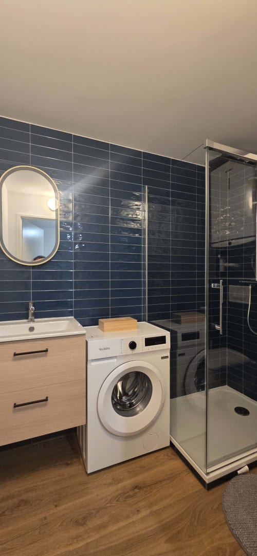 Salle de bain moderne de l'appartement L'Entre-Deux de NN Patrimoine à Douvaine, avec carrelage bleu foncé, lave-linge blanc et bois