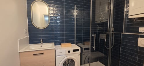 Salle de bain moderne chez NN Patrimoine avec lave-linge, lavabo, miroir ovale et douche aux carrelages bleu foncé à Douvaine