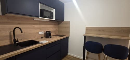 Kitchenette moderne aux armoires foncées, plan de travail en bois, évier noir et coin bar dans l'appartement NN Patrimoine