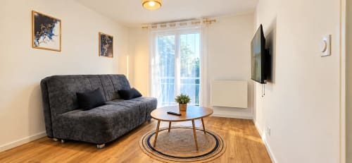 Salon moderne de l'appartement NN Patrimoine avec canapé gris, table en bois, télévision et balcon avec vue sur la ville à Douvaine