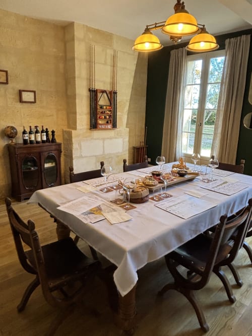 Elegante comedor del Château Alto Cormeil con mesa vestida, botellas de vino y lámparas colgantes de latón en Saint-Émilion