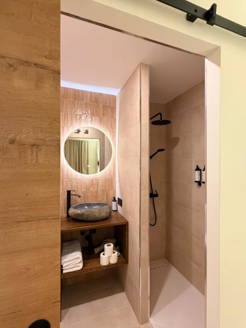 Baño moderno en Tinto Dreams Hostel Haro con lavabo de piedra, espejo iluminado, ducha abierta y mueble de madera