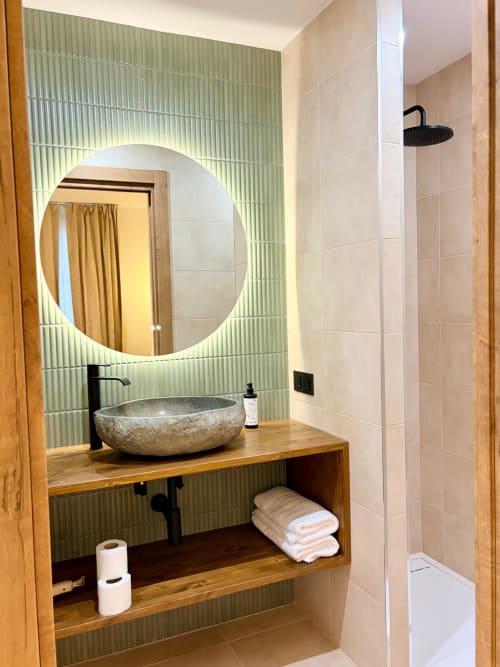 Baño moderno en el Hostel Tinto Dreams de Haro con lavabo de piedra, espejo circular iluminado y ducha a ras de suelo