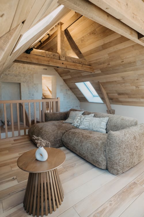 Cozy attic suite at Le Clos d'Omaha with exposed wooden beams, beige sectional sofa, skylight, and wooden coffee table