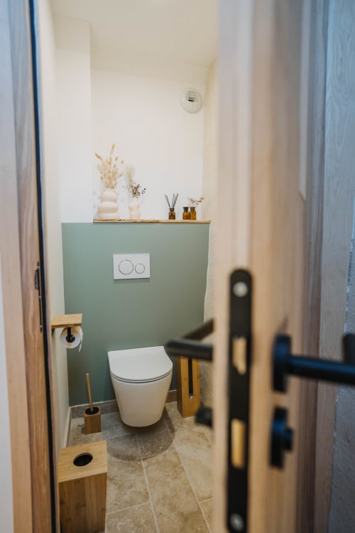 Modern bathroom in Suite Lushoto at Le Clos d'Omaha hotel with sage green accent wall, white toilet, and minimalist décor