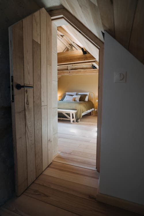 Wooden door opens to Suite Lushoto bedroom at Le Clos d'Omaha, revealing bed with pillows and warm lighting