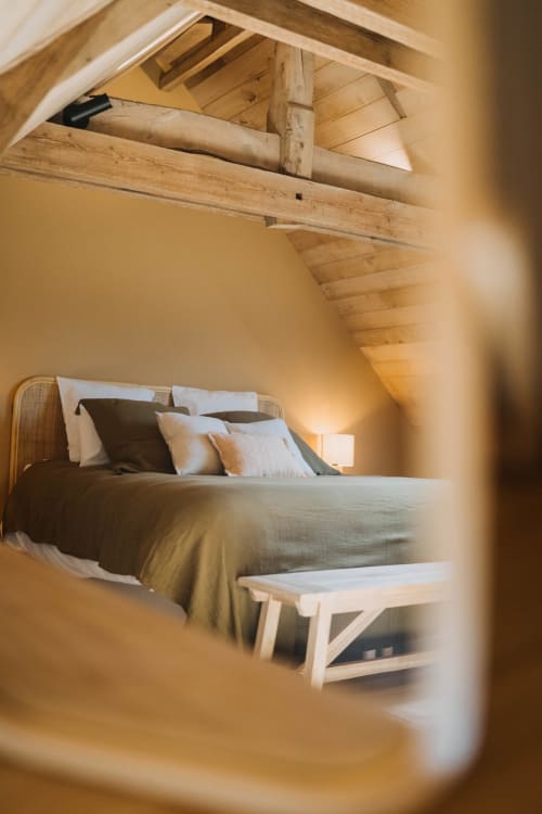 Cozy loft bedroom at Le Clos d'Omaha with wooden beams, bed with pillows, and white bench in Normandy hotel suite