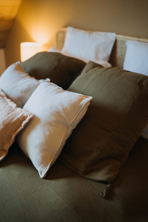 Cozy bed with white and olive pillows at Le Clos d'Omaha hotel suite in Normandy