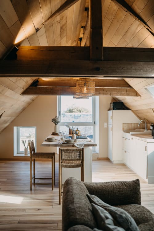 Bright attic suite at Le Clos d'Omaha with exposed beams, wooden floors, dining area, and modern kitchenette overlooking