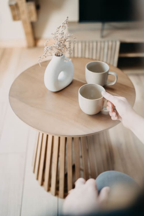 Round wooden table at Le Clos d'Omaha hotel with white ceramic mugs and dried flowers in vase