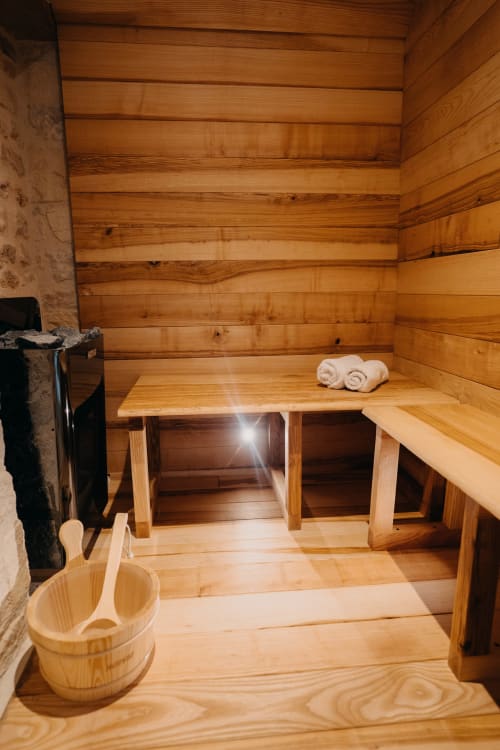 Wooden sauna interior at Le Clos d'Omaha hotel with benches, bucket, and rolled towels
