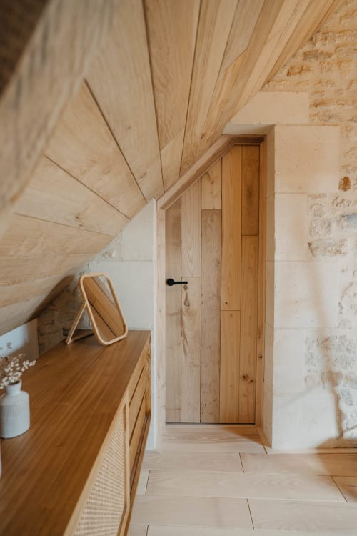 Modern wooden bedroom at Le Clos d'Omaha with sloped ceiling, wooden door, and rustic stone walls