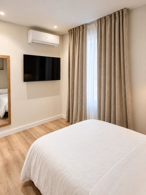 Habitación moderna en Tinto Dreams Hostel, Haro, con cama blanca, TV de pared, cortinas beige y aire acondicionado