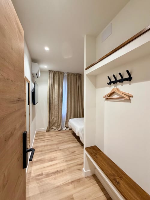 Moderna habitación individual en el Hostel Tinto Dreams de Haro con suelos de madera, cama, armario y balcón con vistas a la ciudad