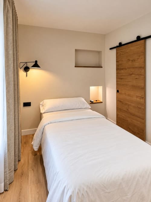 Dormitorio moderno en Tinto Dreams Hostel de Haro con ropa de cama blanca, puerta corredera de madera e iluminación de aplique