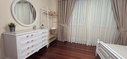 Elegante dormitorio en Casa Amma, Monforte de Lemos, con cómoda blanca, espejo redondo, suelos de madera oscura y cortinas translúcidas