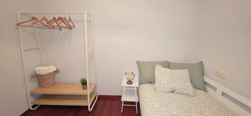 Dormitorio del apartamento Casa Amma con cama, perchero blanco con perchas, estantería de madera y mesita de noche en Bikarte