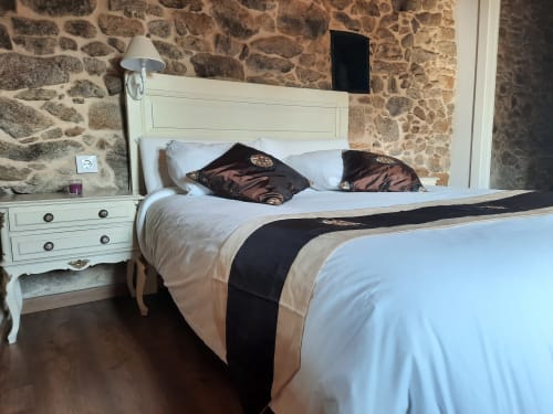 Dormitorio rústico con paredes de piedra, cama blanca, almohadas oscuras, ropa de cama crema y mesita blanca en el hotel Bikarte de Sober