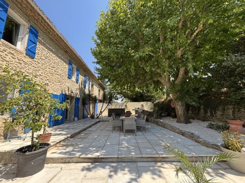 Cour provençale en pierre avec volets bleus, terrasse ombragée et arbres centenaires au Mas Provençal, Bollène