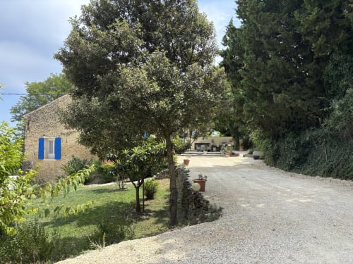 Mas Provençal à Flanc De Colline guesthouse in Bollène with stone building, blue shutters, gravel driveway, and Mediterranean