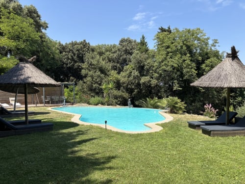 Piscine turquoise avec parasols de paille et transats au Mas Provençal à Bollène, entourée de jardins luxuriants