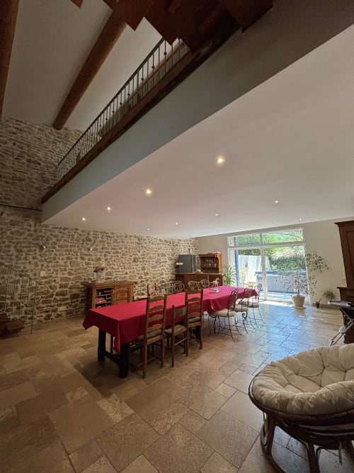 Spacieuse salle à manger du Mas Provençal avec murs en pierre, tables drapées de rouge et poutres apparentes à Bollène