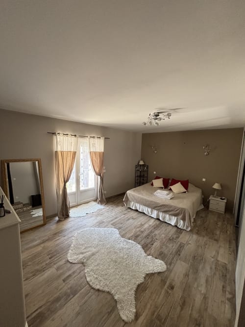 Spacieuse chambre principale au Mas Provençal à Bollène, avec lit, grand miroir, portes vitrées et parquet