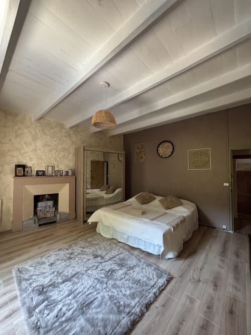 Chambre spacieuse du Mas Provençal avec poutres apparentes, cheminée et luminaire suspendu tressé à Bollène