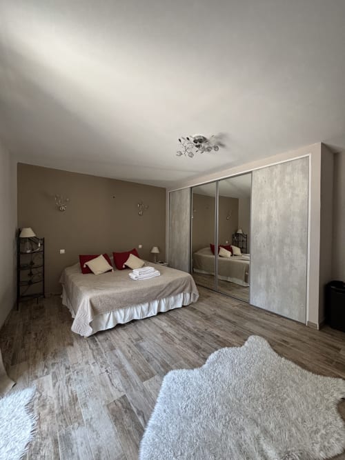 Chambre spacieuse au Mas Provençal avec penderie miroir, literie beige, oreillers rouges, parquet et appliques murales