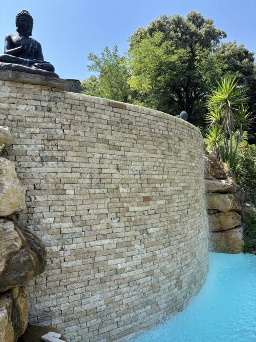 Statue de Bouddha dominant une piscine turquoise et un mur en pierre à Mas Provençal, Bollène