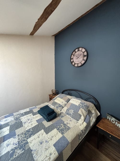 Chambre douillette au Mas Provençal avec mur d'accent bleu, poutres en bois, literie patchwork et horloge vintage à Bollène