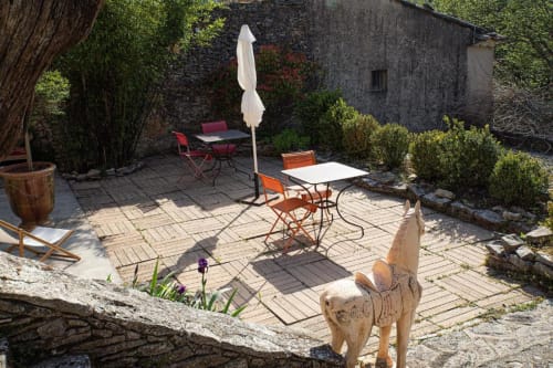 Cour rustique du Clos des Amandiers à Simiane-la-Rotonde : bâtisse en pierre, parasol, chaises de terrasse et chien