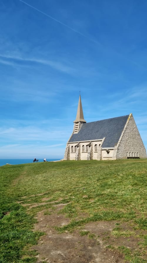 Chapelle de Bon Secours à Étretat dominant la mer avec des prés verts et un ciel bleu clair