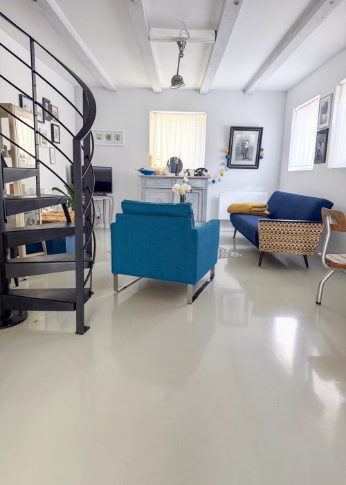 Salon de charme moderne à l'Atelier des Dépendances à Lipsheim avec fauteuils turquoise, escalier hélicoïdal et lumière naturelle généreuse