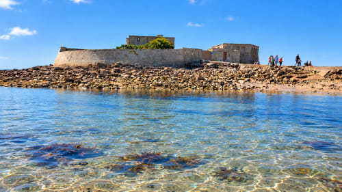 Vue du Fort-Bloqué à Ploemeur, dans le Morbihan, avec ses fortifications en pierre, ses rochers et les eaux transparentes de l'Atlantique.
