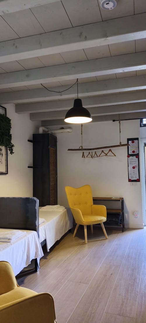 Camera da letto moderna con travi a vista, poltrona gialla e illuminazione a sospensione nel centro di Bergamo