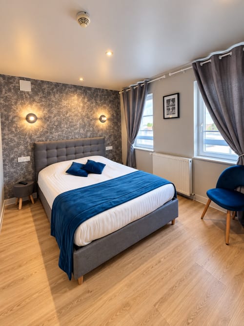 Chambre double moderne à l'Hôtel New Windsor Etretat avec lit rembourré gris, accents velours bleu et papier peint texturé