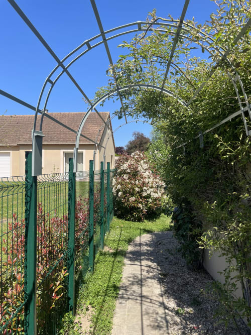 Portail de jardin au Clos d'Émilie avec clôture verte, arbustes en fleur et maison de campagne à Saint-Marcel