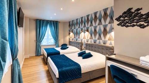 Chambre quadruple moderne à l'Hôtel New Windsor ÉTRETAT avec deux lits doubles, accents bleus et art mural géométrique