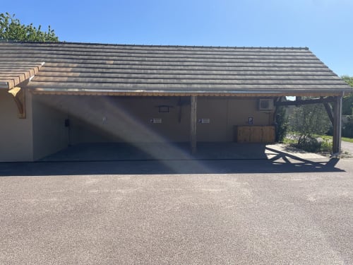 Parking couvert du gîte Le Clos d'Émilie à Saint-Marcel, France, avec toiture en ardoise et accès à la vue sur le jardin