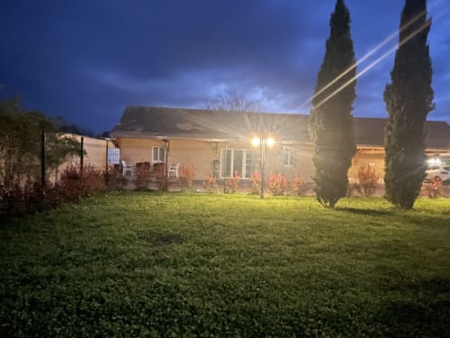 Vue du jardin du Clos d'Émilie au crépuscule avec maison en pierre illuminée, pelouse soignée, cyprès et coin détente