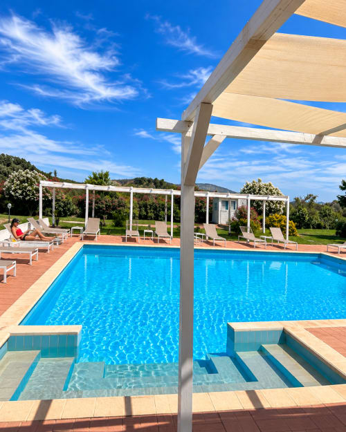 Area piscina del Resort Baia Cea a Bari Sardo con lettini, pergolato ombreggiato e vista sulle montagne sotto cielo azzurro