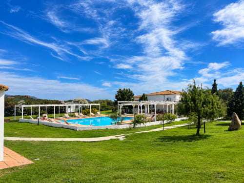 Lussuosa area piscina di Resort Baia Cea con pergolati bianchi, piscina turchese, prato curato e architettura mediterranea