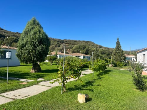 Giardini rigogliosi di Resort Baia Cea a Bari Sardo con cipressi, edifici bianchi e cielo azzurro