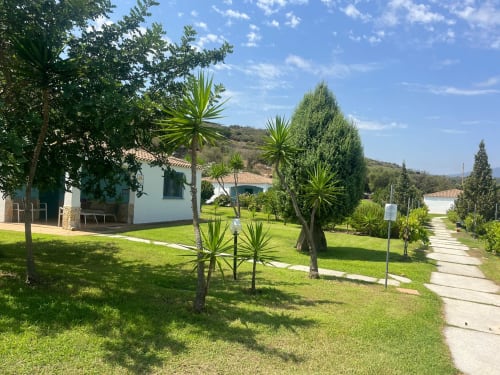 Resort Baia Cea con lussureggianti giardini, palme, cottage bianco, sentiero e colline a Bari Sardo